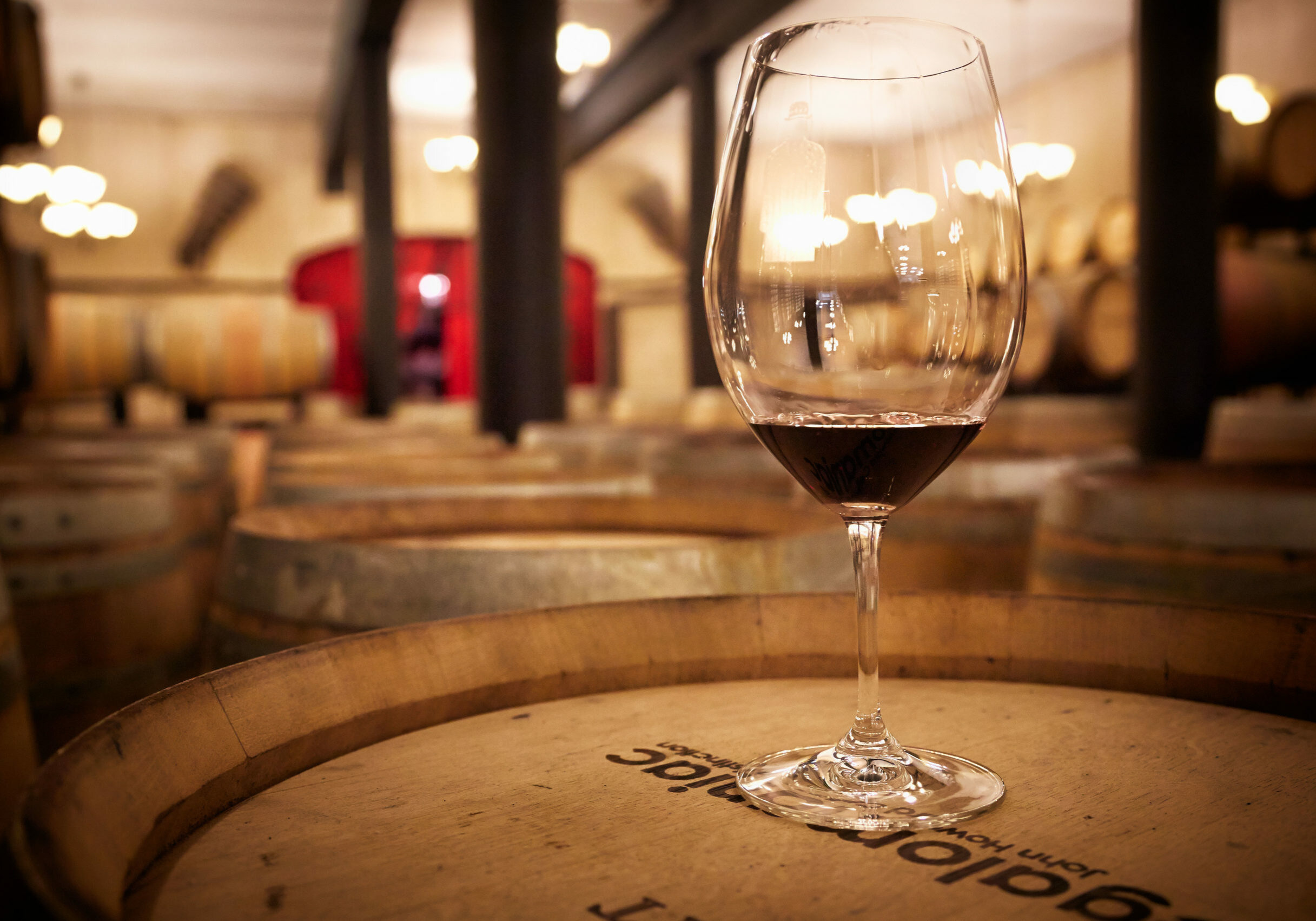 Wine glass on top of a wine barrel in a room filled with wine barrels
